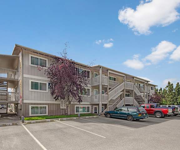 The gray exterior of the apartment buildings with stairs surrounded by greenery and trees with a parking lot in front at Terrace on the Lake Apartment Homes. 