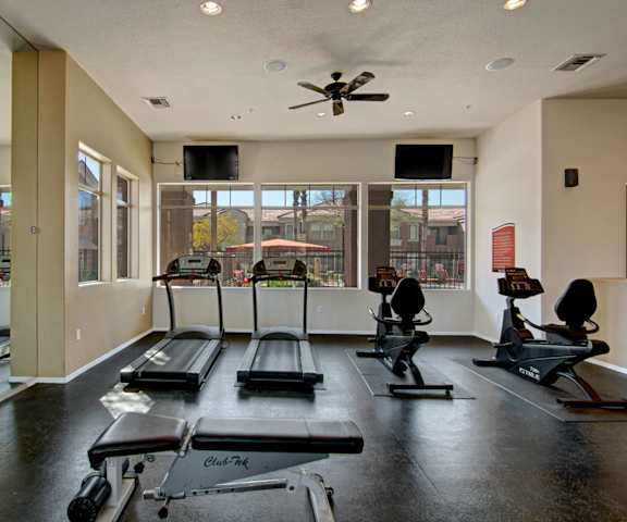 A gym with cardio machines, TVs, and a window view of a pool at Dobson Towne Centre. 