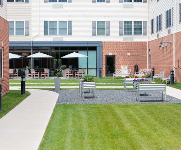A courtyard with a white pathway, a grassy area, and a building in the background.