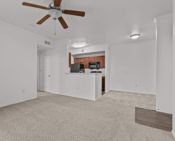 A room with a ceiling fan and a kitchenette in the background.