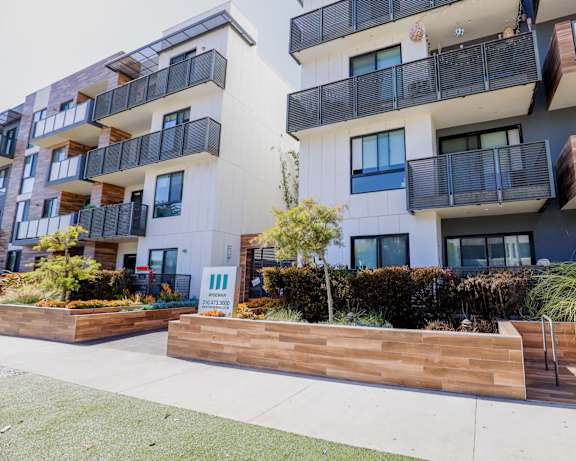 A modern apartment building with balconies and a wooden fence in front.