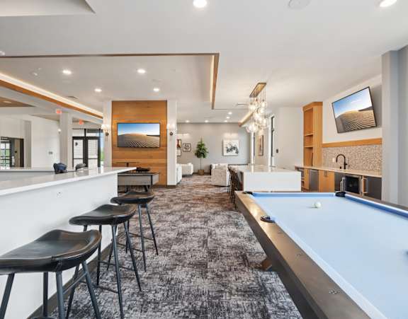A pool table is in the middle of a room with a bar and a TV.