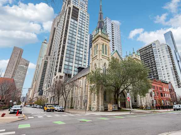 A church with a tall steeple stands in front of a row of modern buildings.
