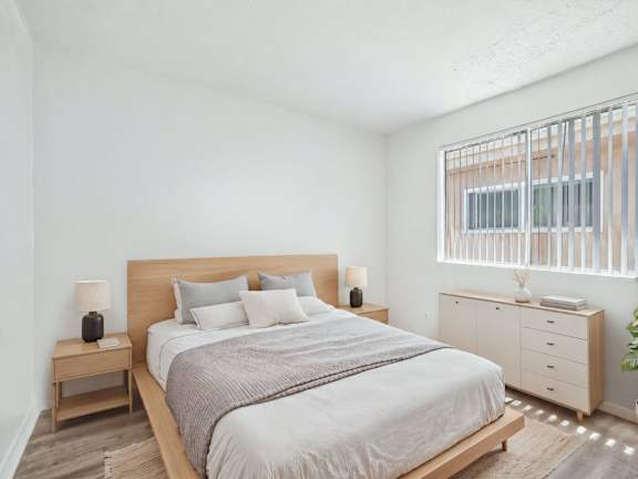 A bedroom with a large bed, a nightstand, and a plant.
