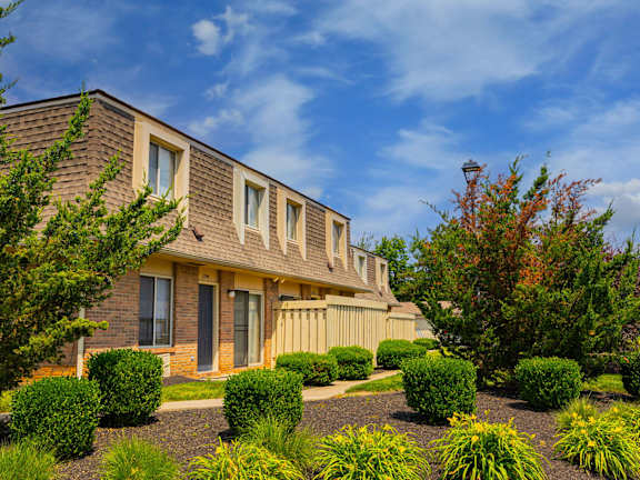 A house with a brown roof and a grey door surrounded by bushes and trees.