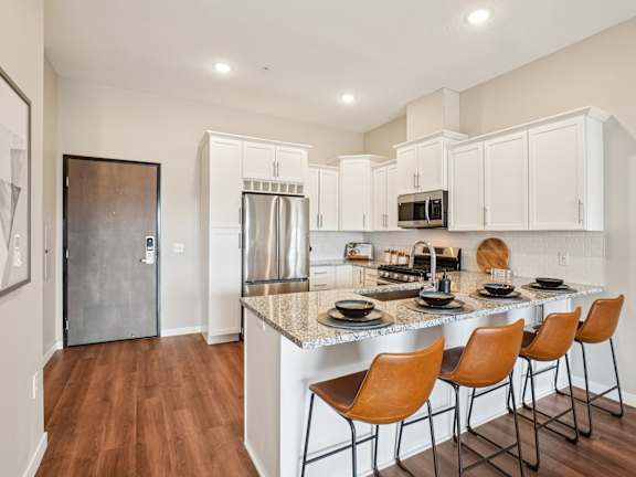 A kitchen with a white counter top and brown chairs.