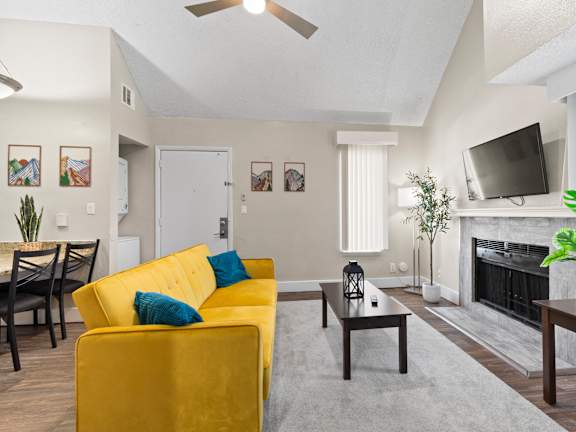 A living room with a yellow couch and a fire place with a TV over it at Fusion Orlando furnished apartments.