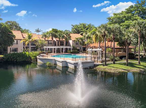 A fountain in the middle of a pond in front of a building.
