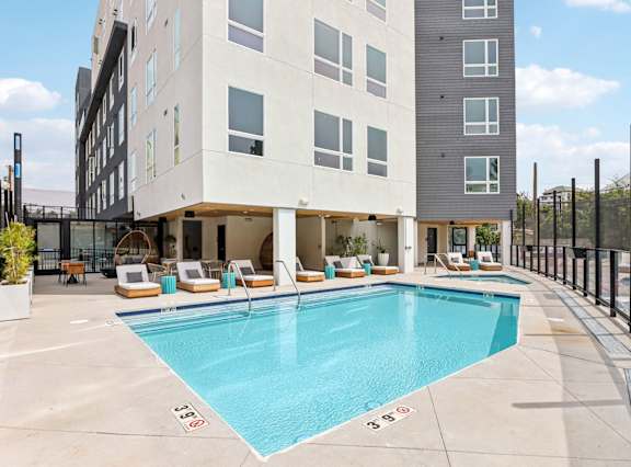 A large swimming pool is surrounded by lounge chairs and a building.
