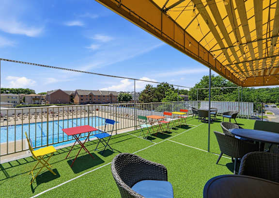 A yellow umbrella shades a table and chairs on a lawn next to a pool.