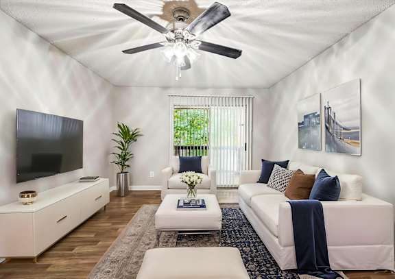 A living room with a white couch, a television, and a ceiling fan.