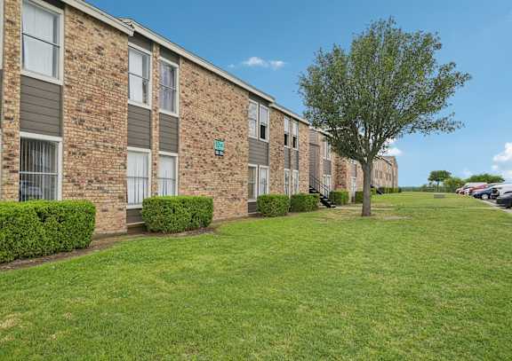 A tree stands in a grassy area in front of a brick building.