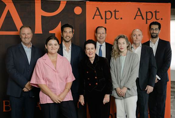 A group of people are standing in front of a sign that says Apt. Apt.