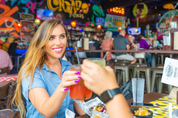 a woman sitting at a table in a restaurant holding up a drink