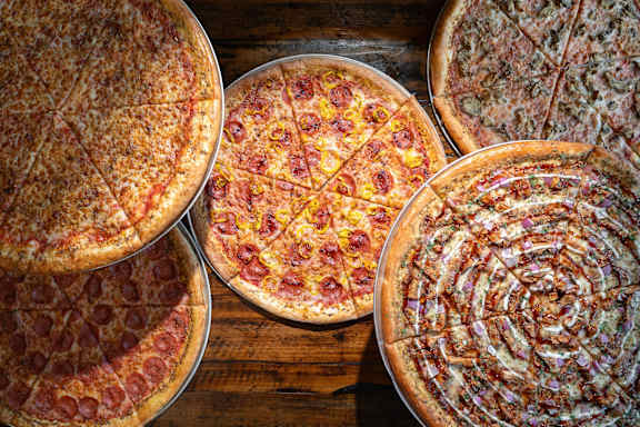 Four pizzas with different toppings are displayed on a wooden surface.