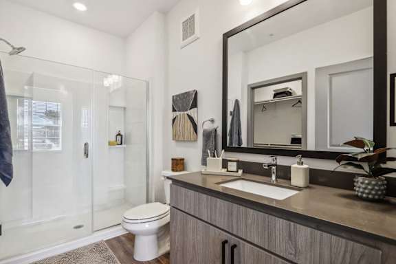 A modern bathroom with a toilet, sink, and mirror. at Stella Luxury Apartment Homes in San Tan Valley, AZ