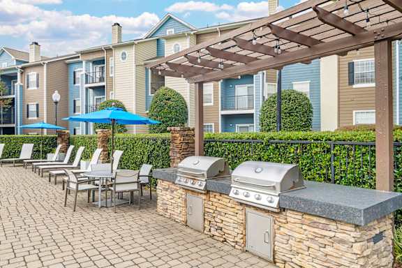 A patio with a grill and chairs under a pergola.