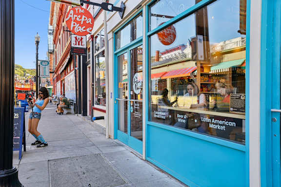 A woman is rollerblading down a sidewalk in front of a store with a sign that says "Latin American Market.".