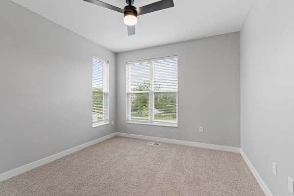 A room with a ceiling fan and two windows.