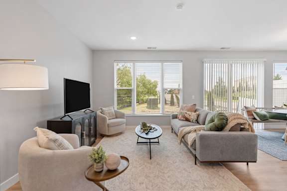 A living room with a grey couch, a white armchair, a coffee table, and a flat-screen TV.