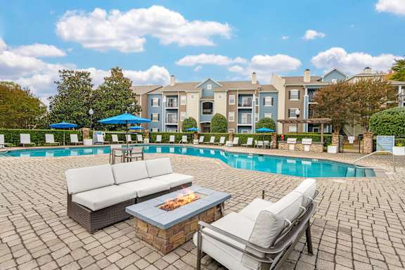 A poolside area with a couch, chairs, and a fire pit.
