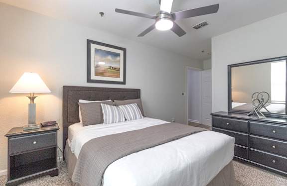 A bedroom with a large bed, a ceiling fan, and a painting on the wall.
