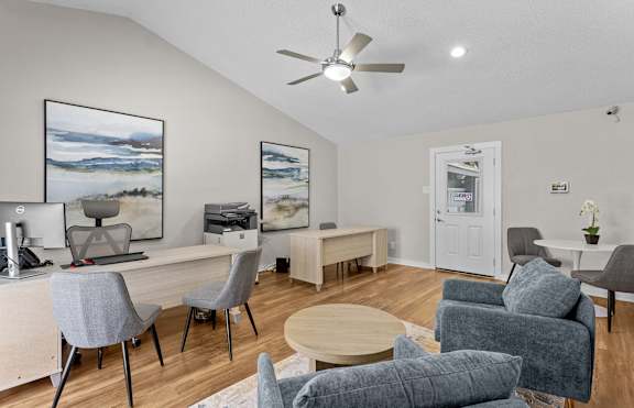 A room with a desk, chairs, and a ceiling fan.