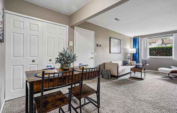 Living room with tan carpet and grey walls. A couch is up against the wall with two chairs under the window. A white dresser is across from the couch.