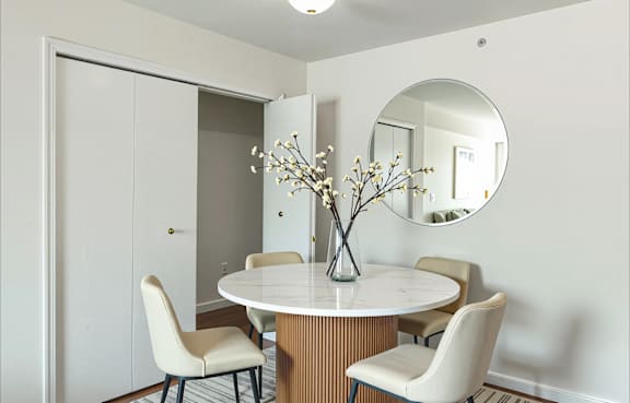 A white table with a vase of flowers on it and four chairs around it.