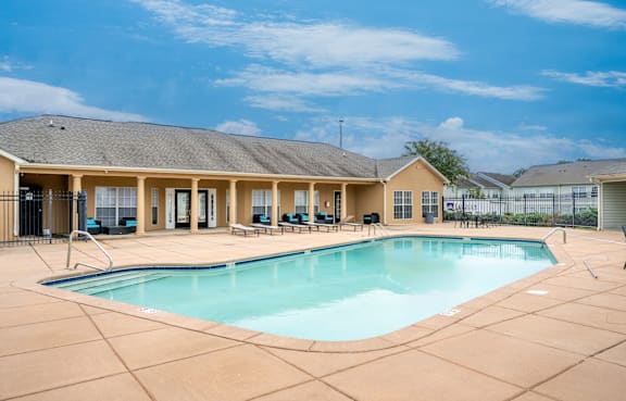 A large swimming pool is surrounded by a concrete patio and a building with a covered patio area.