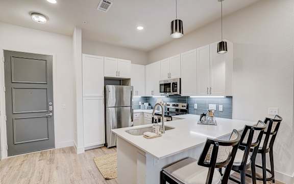 A kitchen with white cabinets and a white island with three chairs.