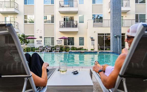 Two people are sitting by a pool with a glass of wine.