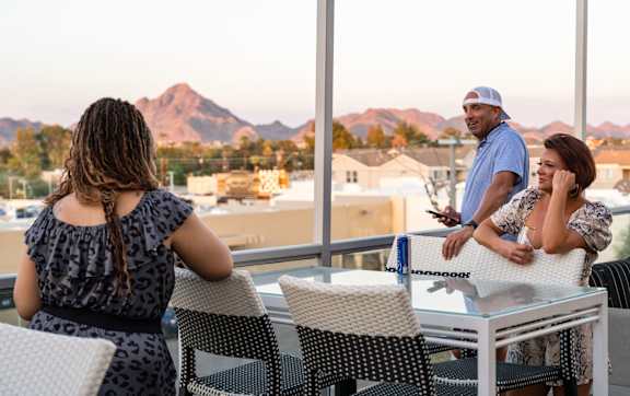 A woman with braided hair is sitting at a table with two other people, looking out at a cityscape.