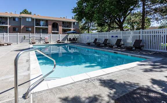 A pool surrounded by a white fence and chairs.