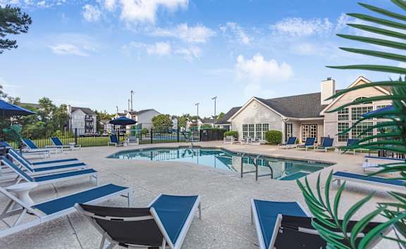 A pool surrounded by lounge chairs and a house in the background.