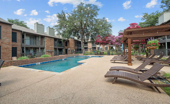 a swimming pool with chaise lounge chairs and a pergola in front of a brick