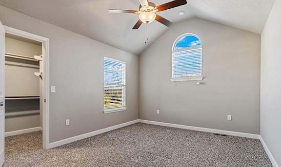 A room with a ceiling fan and two windows.