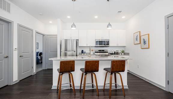 A kitchen with white cabinets and a white island with two bar stools.