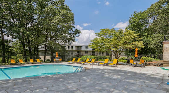 A round swimming pool surrounded by yellow chairs and trees.