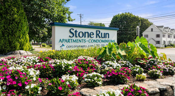 A sign for Stone Run Apartments is surrounded by flowers.