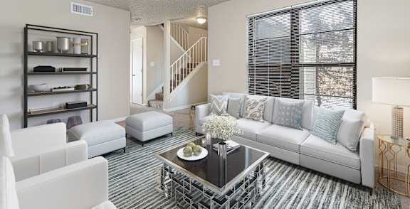 A living room with a white couch, a coffee table, and a staircase in the background.