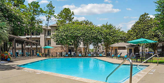 A large swimming pool surrounded by trees and a building in the background.