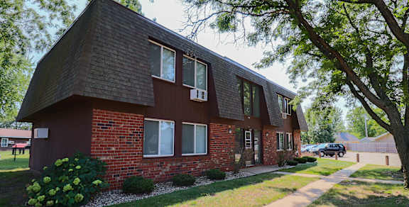 A red brick house with a black roof and a tree in front.