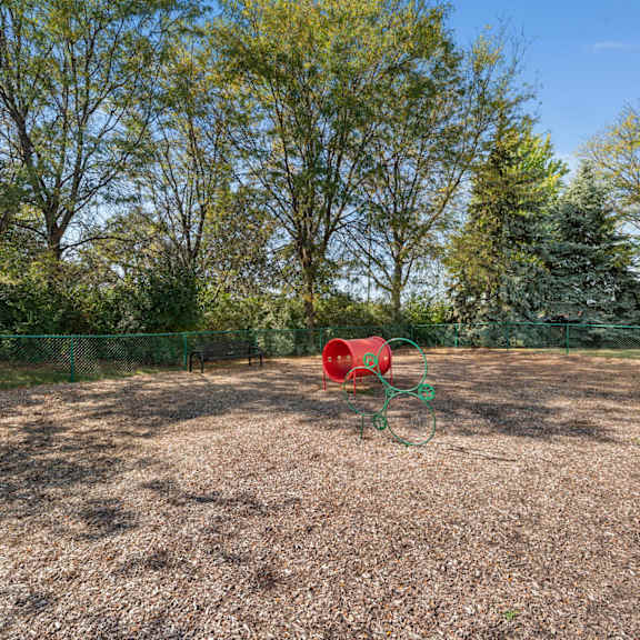 a fenced in play area with a red barrel and other playground equipment
