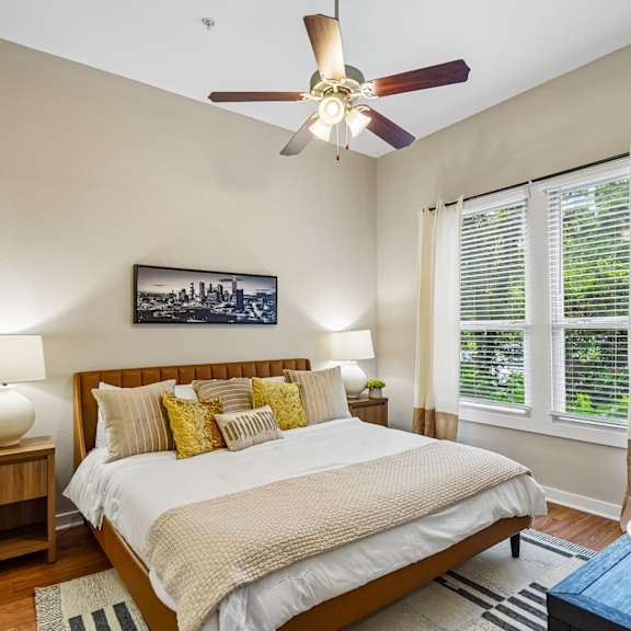 A bedroom with a large bed, a ceiling fan, and a painting on the wall.
