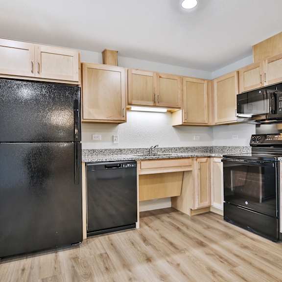 A black refrigerator is in a kitchen with wooden cabinets.