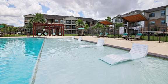 A swimming pool with a few chairs and a building in the background.