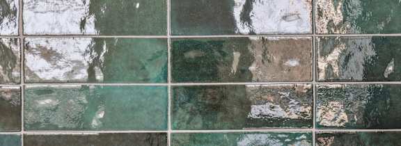 A wall made of square tiles with a mix of green and brown hues.