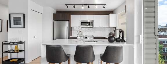 a kitchen with white cabinetry and a large island with three stools in front of it