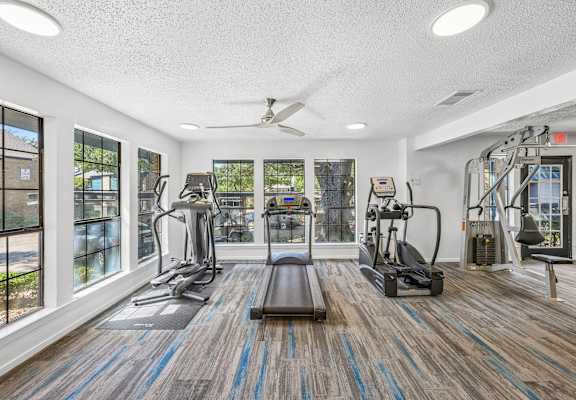 A gym with a variety of equipment including treadmills, weights, and a bench.
